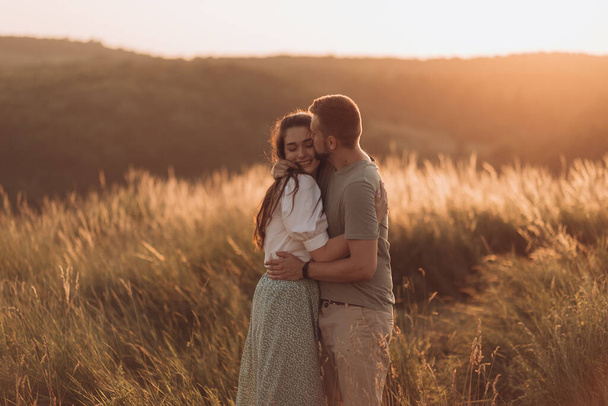 Młoda szczęśliwa para w miłości przytula i pięknie trzyma się za ręce w górach zachodzącego słońca - Zdjęcie, obraz