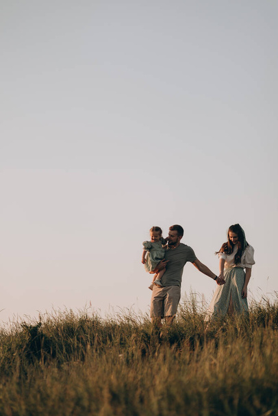 幸せな家族は日没時に公園を歩く。ママとパパと赤ちゃん。健康的な家族が畑で遊んでいます。幸せな家庭のコンセプト - 写真・画像