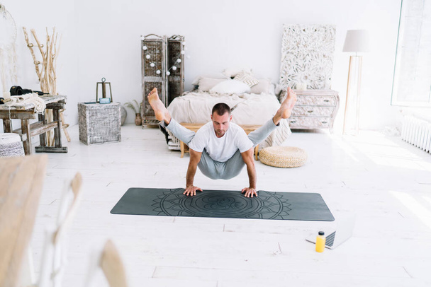 Handsome strong caucasian male using laptop computer for watching lessons of yoga staying at home, pensive 20s hipster guy on carpet standing in asana recreating and keeping fit in retreat - Fotografie, Obrázek