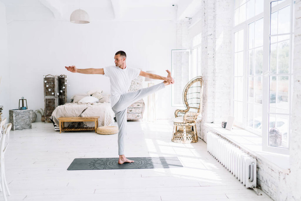 Full body barefoot concentrated male in sportswear performing yoga pose on mat while practicing Revolved Standing Hand to Toe pose - Fotoğraf, Görsel