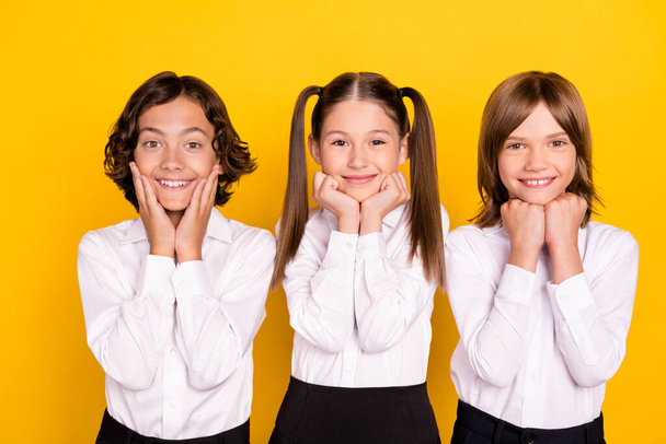 Photo of three adorable schoolkids hands cheeks smile wear white shirt isolated yellow color background - Zdjęcie, obraz