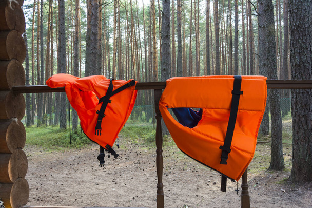 children's and adult bright orange life jackets hang on the railing of a forest house. - Foto, Imagen
