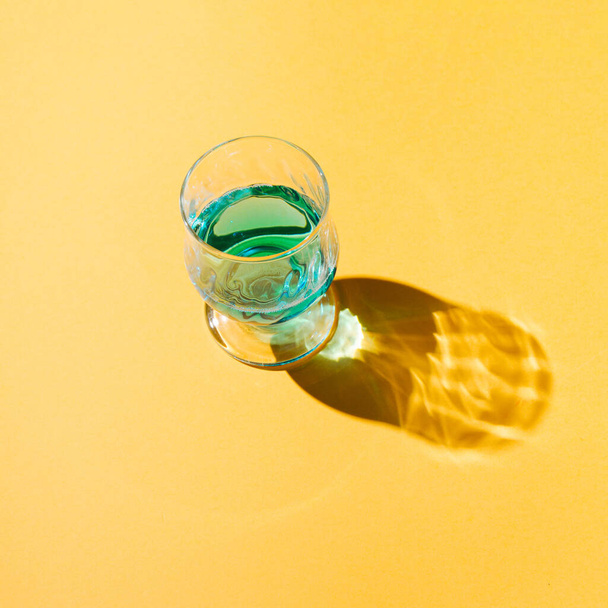Authentic sunlit summer idea with a glass of drink on a pastel yellow background. Creative minimal concept. - Foto, Imagem