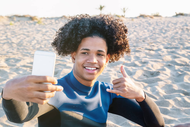 Nuori afroamerikkalainen mies istuu hiekalla ottaa kuvan älypuhelimella - Valokuva, kuva