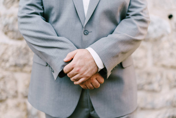 Een man in een grijs pak kruiste zijn armen over zijn buik. Close-up - Foto, afbeelding
