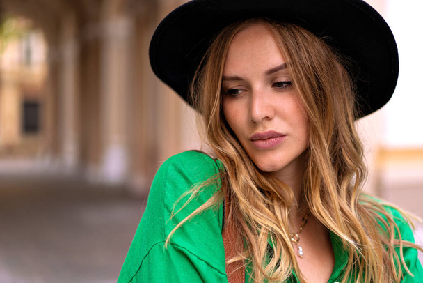 Close up portrait of elegant stylish woman with blonde curly hairs freckle face and natural make up, wearing black fedora posing on the street. - Foto, imagen