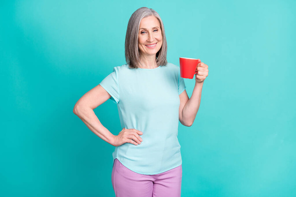 Photo of pretty charming good mood smiling mature woman drinking warm coffee isolated on teal color background - Photo, Image