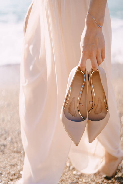 彼女の手に靴を持つ花嫁はビーチに沿って歩く。閉鎖 - 写真・画像
