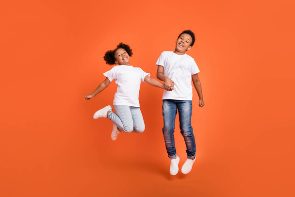 Full size photo of small funny girl boy jump wear white t-shirt jeans sneakers isolated on orange background - Fotografie, Obrázek