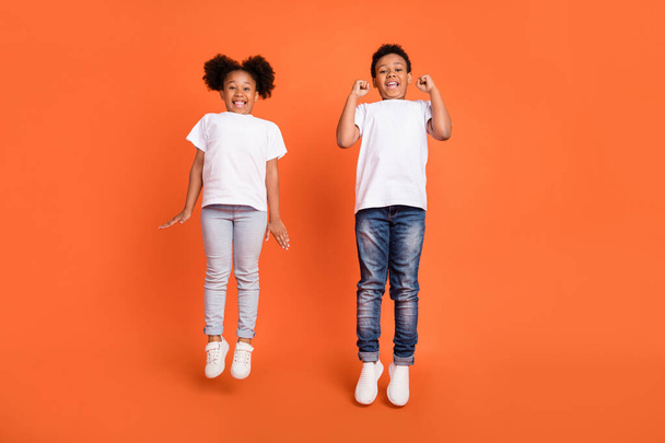Full length photo of little hooray girl boy jump wear white t-shirt jeans sneakers isolated on orange background - Foto, afbeelding