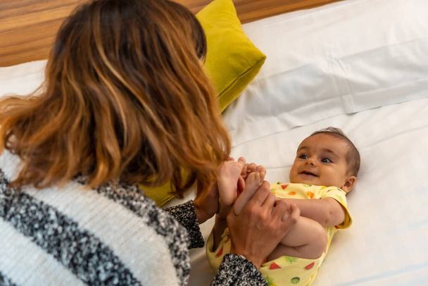 Detail of a young mother having fun with her baby on the bed in her bedroom, young Caucasian first-time with her four-month-old baby, family at home - Foto, Bild