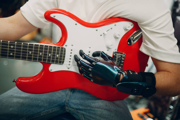 Молодой инвалид с искусственным протезом руки играет на гитаре в магазине. - Фото, изображение