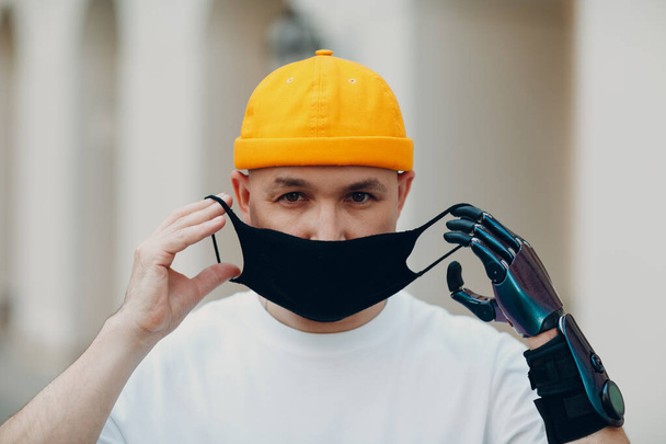 Young disabled man put on medical protective face mask with artificial prosthetic hand. - Photo, Image