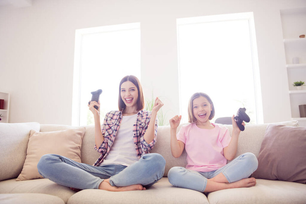 Portrait of two attractive cheerful girls sitting on divan playing video game having fun at home flat indoors - Foto, afbeelding