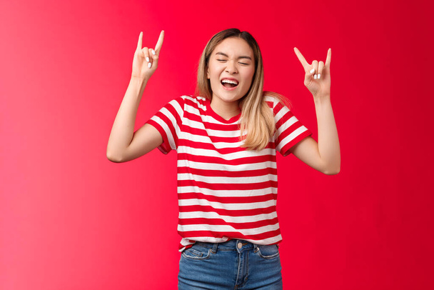 Upbeat wild reckless blond asian girl having fun losing control, showing rock-n-roll sign enjoy awesome party yelling singing along cool concert, heavy metal sign close eyes, stand red background - Photo, Image