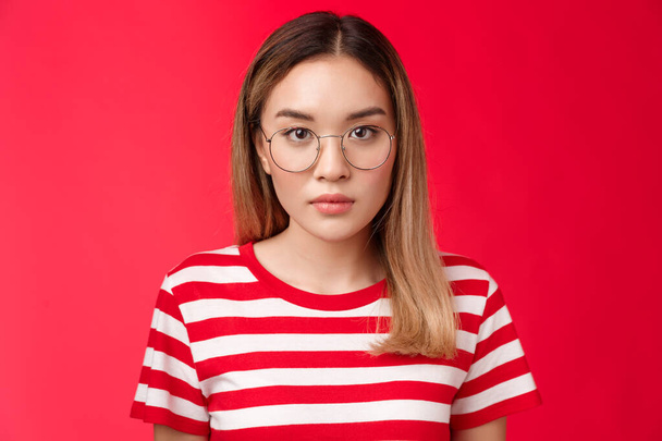 Primer plano serio enfocado inteligente asiático joven estudiante escuchar cuidadosamente lectura look cámara concentrado desgaste prescrita gafas stand rayas camiseta rojo fondo - Foto, Imagen