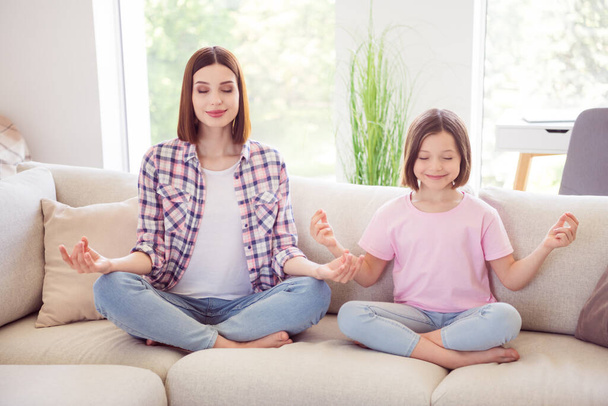 Pełna długość zdjęcie szczęśliwego spokojnego rodzeństwa siostry siedzieć sofa medytacja wewnątrz domu - Zdjęcie, obraz