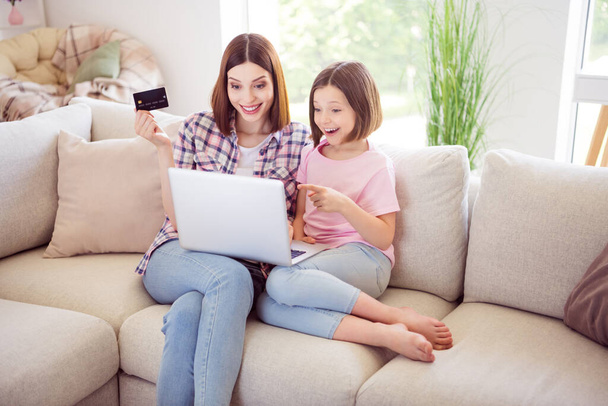 Photo of happy people brunette sisters sit sofa look laptop point finger hold credit card indoors inside house home - Foto, Imagem