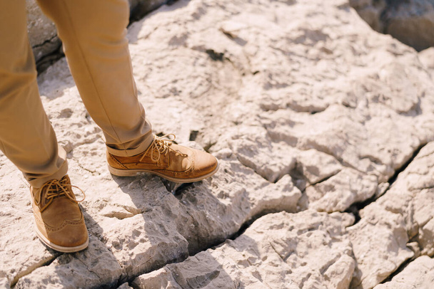 Αρσενικά πόδια με καφέ παντελόνια στο βράχο. Κοντινό πλάνο - Φωτογραφία, εικόνα