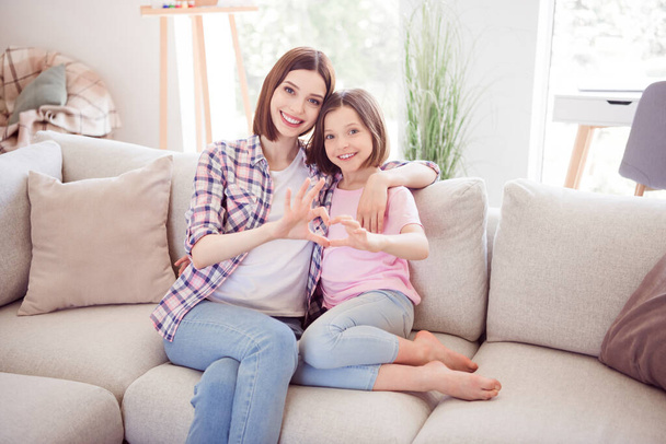 Portrait of two attractive cheerful affectionate girls spending time showing heart sign hugging at home flat indoors - 写真・画像
