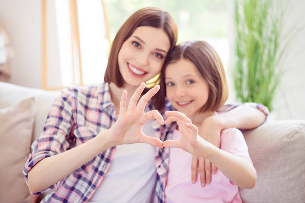 Photo of cheerful happy positive sisters smile make fingers heart shape harmony love indoors inside house - Foto, immagini