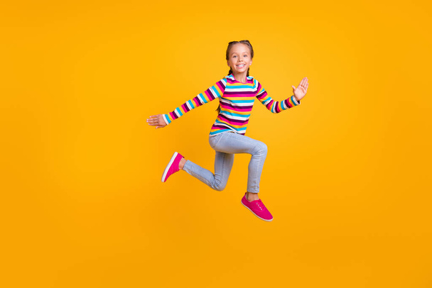 Photo of carefree runner sporty girl jump hurry fast wear striped shirt jeans shoes isolated yellow color background - Foto, Imagem