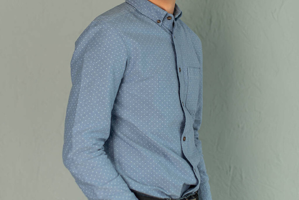 Ένας νεαρός άνδρας με μπλε πουκάμισο και στέκεται σε γκρι φόντο. - Φωτογραφία, εικόνα