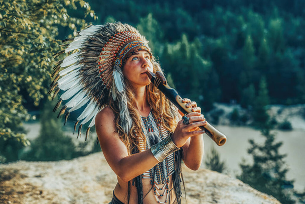 beautiful shamanic girl playing on shaman flute in the nature. - Photo, image