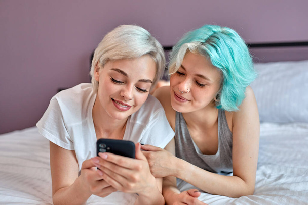 Two young attractive women lying at home on bed with smartphone, having fun - Photo, image