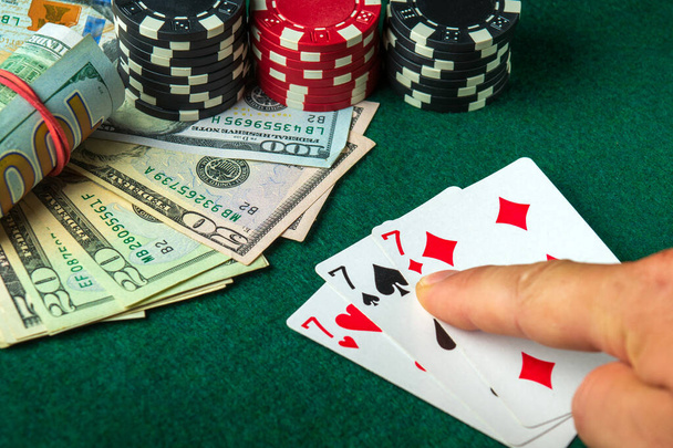 Игрок указывает пальцем на выигрыш тройки или комбинацию наборов в игре в покер на столе с фишками и деньгами в казино - Фото, изображение
