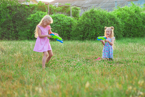 dwie dziewczynki bawią się latem na zielonej łące z pistoletami wodnymi - Zdjęcie, obraz