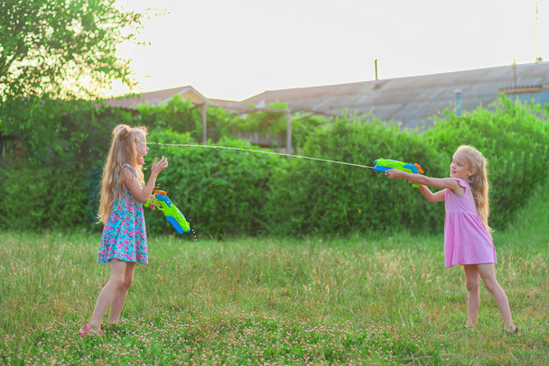 two little girls play in the summer on a green meadow with water pistols - Foto, afbeelding