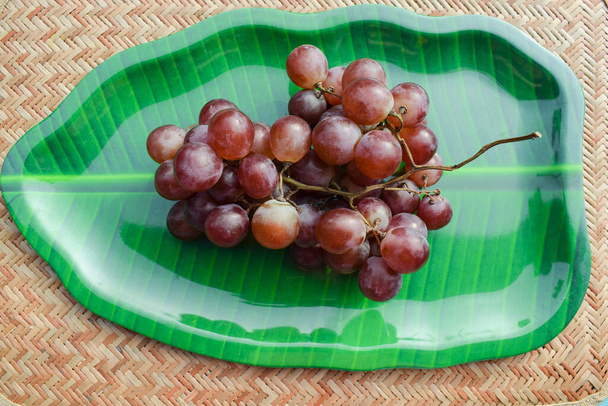 Красивая связка красного винограда большого размера сладкий виноград со стеблем импортируется в Индию Азии. Виноград подается на подносе для листьев тарелок - Фото, изображение