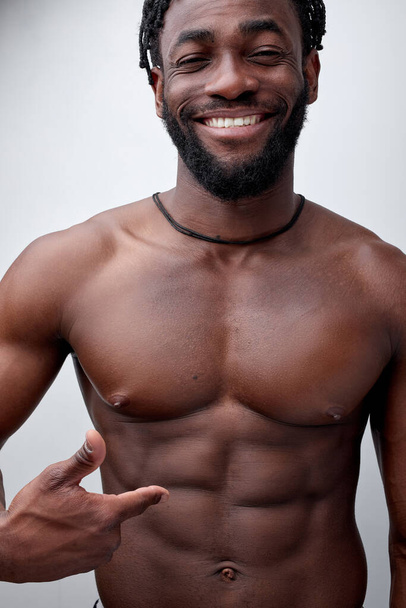 Positive smiling african bodybuilder showing at abdominal abs, shirtless muscular body - 写真・画像