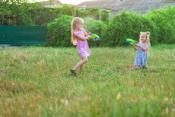 deux petites filles jouent en été sur une prairie verte avec des pistolets à eau - Photo, image