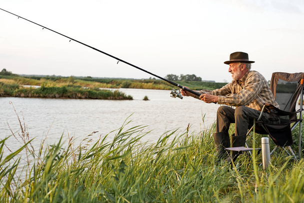 Side view on elderly man fishing on lake in nature, patience and recreation concept - Photo, image