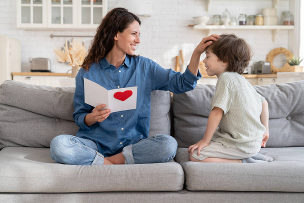Boldog egyedülálló anya megérint gyerek haj tartalmas ajándék, anya ül a kanapén kisfiúval tartsa üdvözlő kártya - Fotó, kép