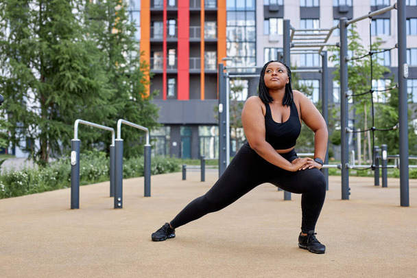 focused fat woman in black tracksuit is engaged in fitness on sports ground, side view portrait - Photo, Image
