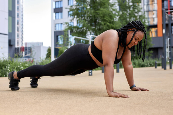Sporty obese woman in black sportswear, practicing fitness, doing Push ups or press ups - Foto, Bild