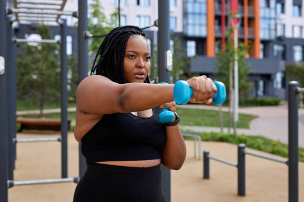 Portrait of young confident african woman exercising with dumbbells - 写真・画像