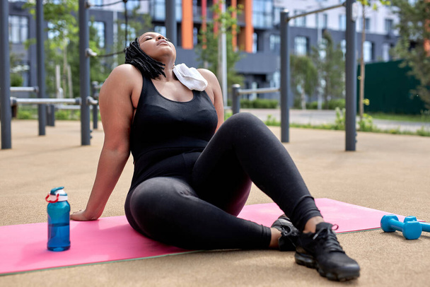 Tired obese afro female having rest on fitness mat after workout, take a break - Foto, imagen