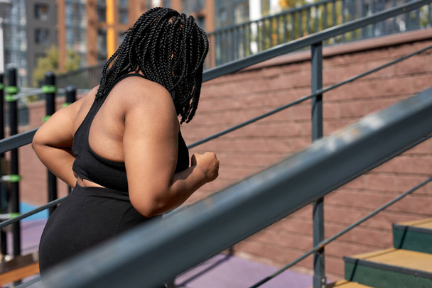 Gruba młoda Afrykanka przeciwstawia się ćwiczeniom fitness na schodach na świeżym powietrzu. utrata masy ciała - Zdjęcie, obraz