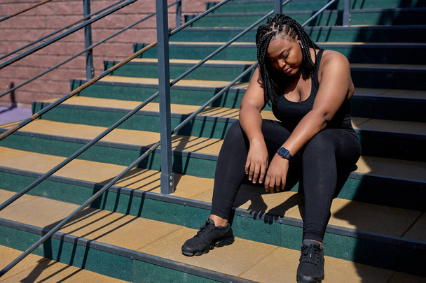 Very Exhausted Black Woman In Black Tracksuit Sitting On Stairs Having Rest, Sport - Φωτογραφία, εικόνα