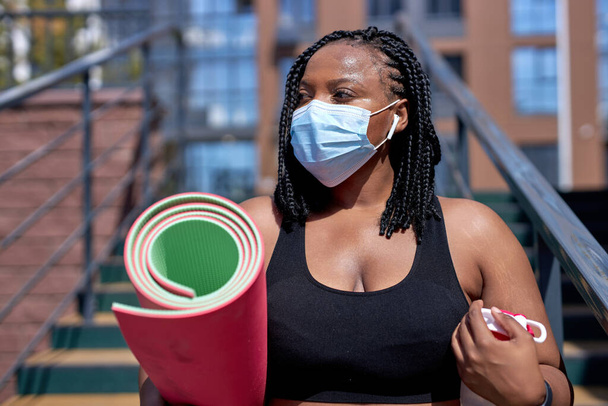 Confident Black Mixed Race Female With Fitness Mat In Hands In Medical Mask Outdoors - Zdjęcie, obraz