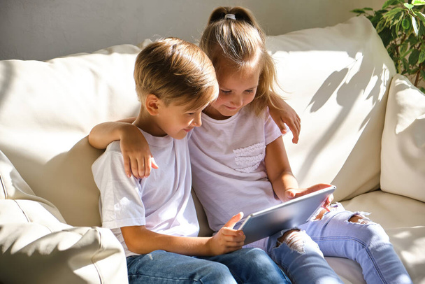 rodina, děti, technologie a domácí koncept - usmívající se bratr a sestra s počítačem tabletu na pohovce v obývacím pokoji - Fotografie, Obrázek