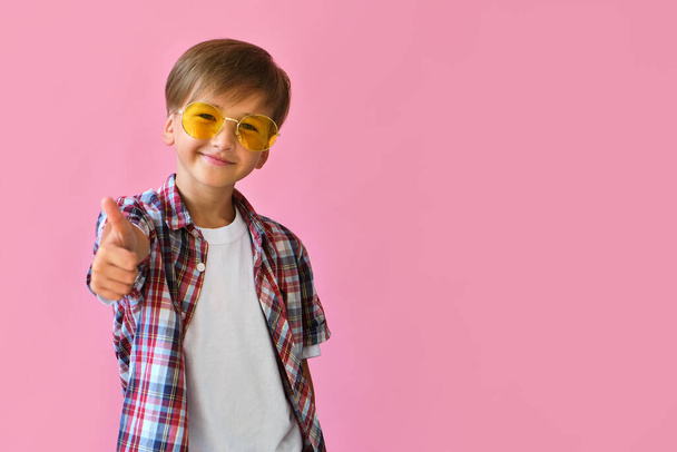 Summer holiday and vacation concept. Happy stylish school boy in yellow sunglasses with thumb up against pink background. Back to school - Foto, Imagen