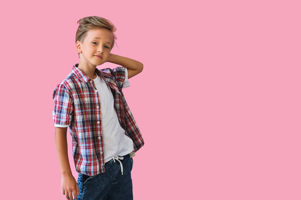 Young stylish handsome kid smiling in a white T-shirt and a plaid shirt. Studio portrait over pink background - Foto, imagen