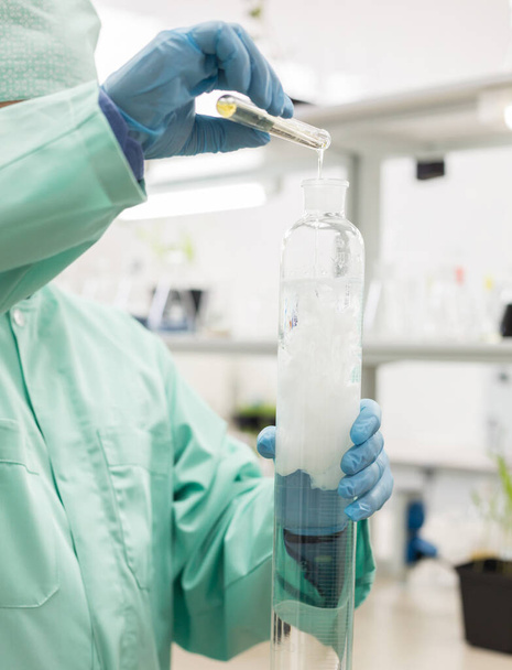 Лаборант наливает жидкость в высокую фляжку на фоне лаборатории. Концепция: Научные исследования в биологии - Фото, изображение