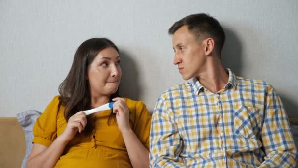 mujer muestra a un hombre el resultado de una prueba de embarazo mientras está sentado en la cama, sorpresa, consideración - Imágenes, Vídeo