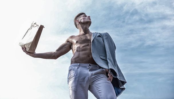 Sales season. Shop assistant concept. Man muscular athlete hold shopping bag sky background. Hot sales and discount. Guy attractive macho carry shopping bag made out of brown paper. Take this package - 写真・画像